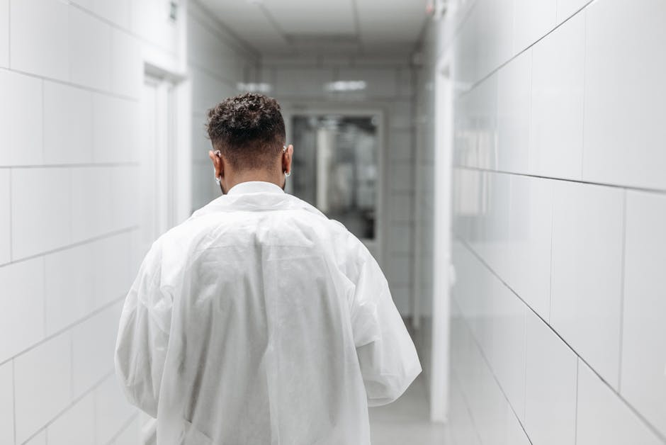 Rear view of a healthcare professional in a lab coat walking along a bright hospital corridor.